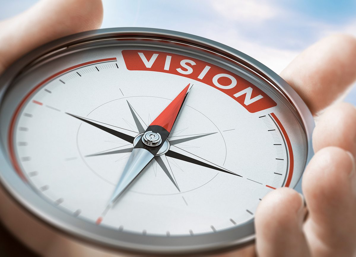 A compass held in cupped hands, its needle pointing to the word Vision